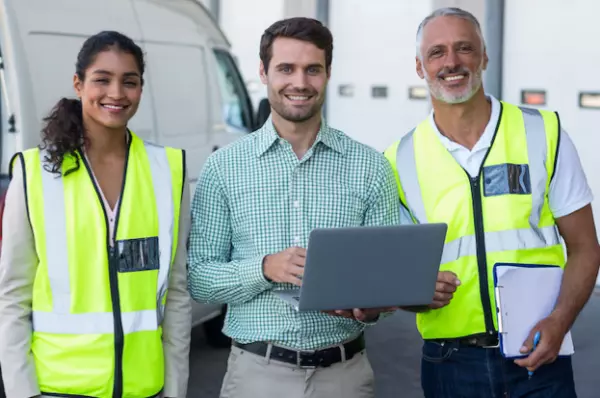 Team of 2 man & 1 woman smiling with a laptop on the hand of 1 person standing in middle 